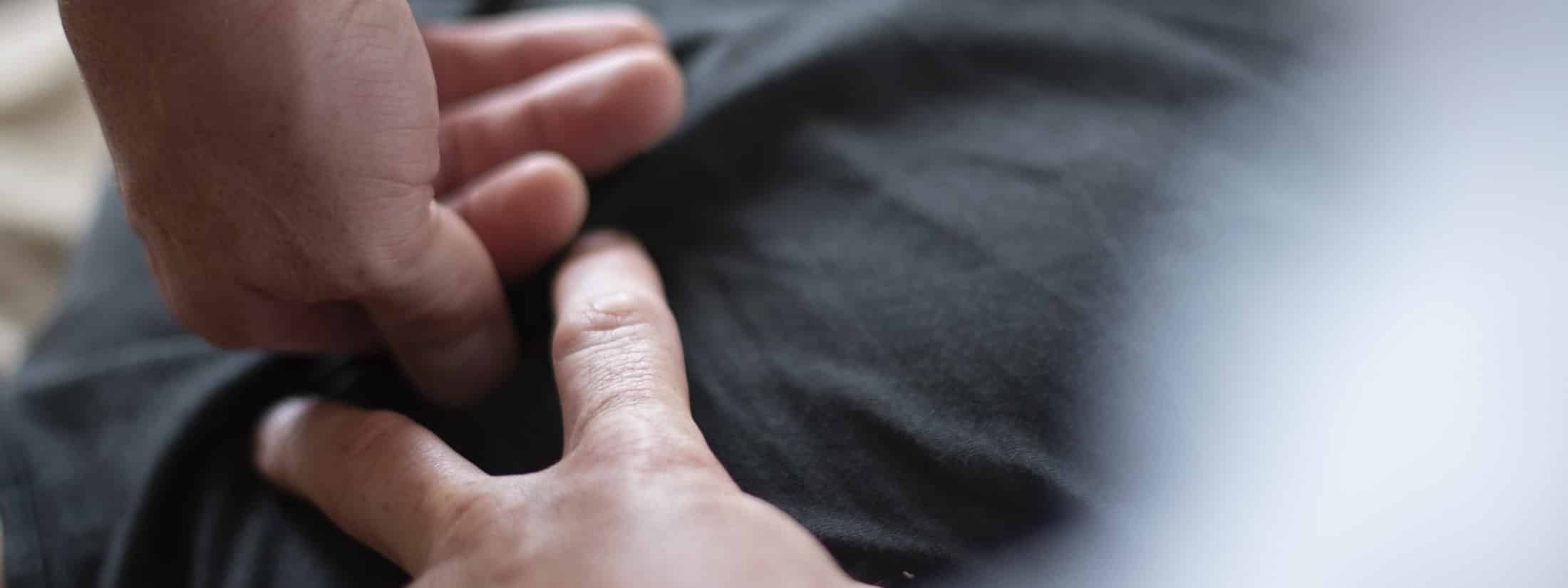 En behandlers hænder arbejder omkring et knæ, tæt på i varmt dagslys